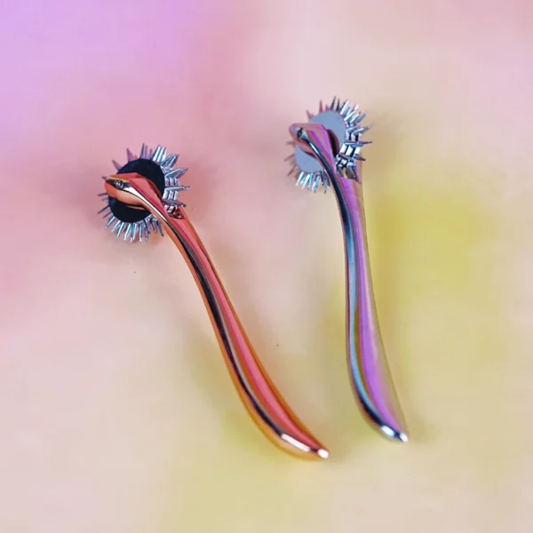 A pair of shiny BDSM rollers are displayed against a soft, gradient background in pastel colors. Each roller features a rounded, spiked head that glistens, showcasing sharp metal points arranged in a circular pattern. The sleek, elongated handles curve gently, reflecting light in vibrant hues, creating an eye-catching visual that highlights the unique design of these BDSM rollers.
