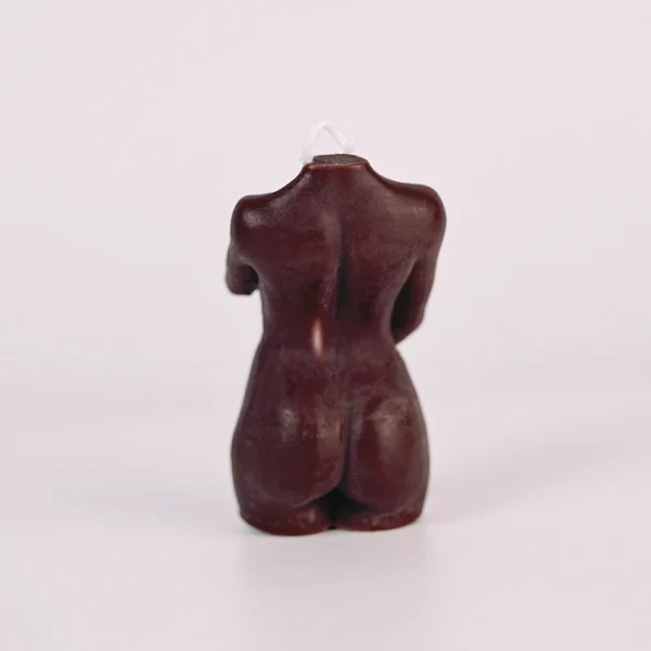 A striking brown candle shaped like the back of a female torso, showcasing intricate details that highlight the contours of the body. The smooth, glossy surface reflects light softly, enhancing its elegant form. A small wick peeks from the top, indicating its functionality as a candle. This artistic piece not only serves as a unique decor item but also creates an inviting atmosphere when lit, embodying the essence of sensual candles. The minimalist background further emphasizes its beauty, making it a perfect addition to any romantic setting.