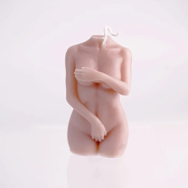 A beautifully crafted candle shaped like a female torso without a head, capturing elegant details of the body in soft, nude tones. One arm delicately crosses over the chest, while the other hand rests just above the thigh, creating an intimate and artistic pose. The smooth surface of the candle catches light gently, enhancing its form and texture. This unique piece not only serves as a decorative element but also adds a warm, inviting glow when lit, embodying the spirit of sensual candles. Its minimalist design stands out against a plain background, making it an ideal addition to any romantic setting.