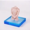 A striking candle shaped like a headless male torso, showcasing well-defined muscles and a smooth, flesh-toned surface. The figure stands with hands clasped in front, positioned on a vibrant blue acrylic base that contrasts beautifully with the candle. This unique design adds an artistic flair to any setting, making it a captivating decor piece. When lit, it not only provides a warm, inviting glow but also embodies the allure and elegance of sensual candles. The minimalist background highlights the candle’s intricate details and soft texture, perfect for enhancing a romantic atmosphere.