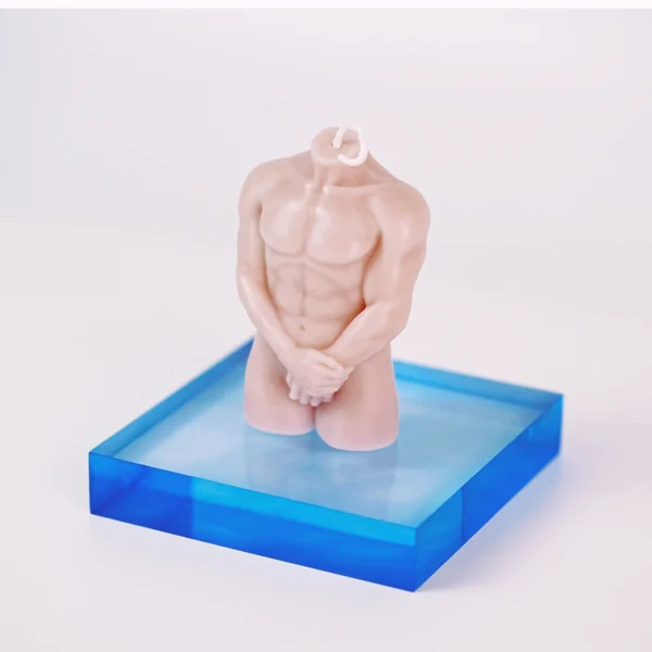 A striking candle shaped like a headless male torso, showcasing well-defined muscles and a smooth, flesh-toned surface. The figure stands with hands clasped in front, positioned on a vibrant blue acrylic base that contrasts beautifully with the candle. This unique design adds an artistic flair to any setting, making it a captivating decor piece. When lit, it not only provides a warm, inviting glow but also embodies the allure and elegance of sensual candles. The minimalist background highlights the candle’s intricate details and soft texture, perfect for enhancing a romantic atmosphere.