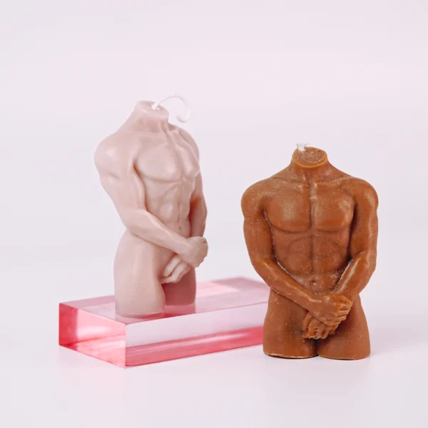 Two artistic candles shaped like headless male torsos, showcasing a range of skin tones. The lighter candle stands on a transparent pink acrylic base, capturing intricate details of well-defined muscles with one hand resting at its waist. Next to it, a darker-toned candle exhibits a similarly muscular form, arms crossed in front, adding a sense of elegance. Both candles are designed to provide a warm glow when lit, doubling as striking decor pieces. These unique creations embody the allure of sensual candles, perfect for enhancing any romantic atmosphere. The minimalist background emphasizes their artistic features.