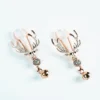 A pair of luxurious nipple clamps featuring a decorative design of deer skulls with antlers, set against a clean white background. The clamps are elegantly crafted in shiny rose gold, embellished with sparkling rhinestones along the antlers. Each clamp is adorned with a small metallic bell that dangles below the skull, adding a playful touch to the sophisticated design, perfect for those exploring role play dynamics.