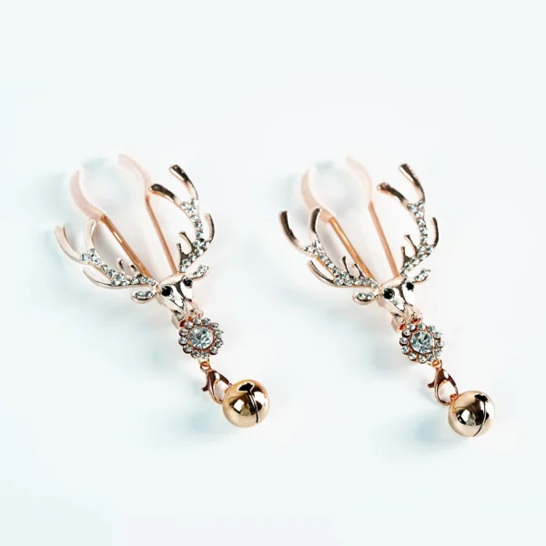 A pair of luxurious nipple clamps featuring a decorative design of deer skulls with antlers, set against a clean white background. The clamps are elegantly crafted in shiny rose gold, embellished with sparkling rhinestones along the antlers. Each clamp is adorned with a small metallic bell that dangles below the skull, adding a playful touch to the sophisticated design, perfect for those exploring role play dynamics.