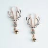 A pair of elegant nipple clamps featuring ornate deer skull designs with sparkling rhinestones. The clamps are crafted in a shiny rose gold color, showcasing antlers that extend outward. Each clamp is adorned with a decorative ball dangling from a link below the skull, adding a playful detail. Set against a clean white background, these nipple clamps combine style and function, perfect for those exploring role play dynamics.