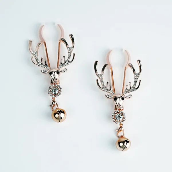 A pair of elegant nipple clamps featuring ornate deer skull designs with sparkling rhinestones. The clamps are crafted in a shiny rose gold color, showcasing antlers that extend outward. Each clamp is adorned with a decorative ball dangling from a link below the skull, adding a playful detail. Set against a clean white background, these nipple clamps combine style and function, perfect for those exploring role play dynamics.