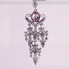 An ornate pair of clamps is displayed against a soft pastel background. The clamps feature elegant silver detailing and shimmering purple gemstones, with a decorative crown-shaped design at the top. Dainty chains drape gracefully, adorned with sparkling accents that catch the light. Rubber tips ensure comfort, making these eye-catching clamps both stylish and functional for those exploring role play dynamics.