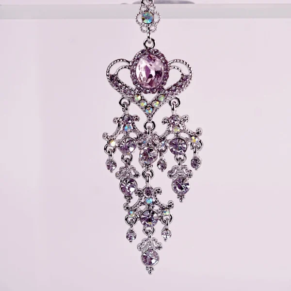 An ornate pair of clamps is displayed against a soft pastel background. The clamps feature elegant silver detailing and shimmering purple gemstones, with a decorative crown-shaped design at the top. Dainty chains drape gracefully, adorned with sparkling accents that catch the light. Rubber tips ensure comfort, making these eye-catching clamps both stylish and functional for those exploring role play dynamics.