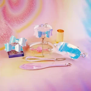 A colorful assortment of playful bondage gear displayed against a soft, pastel backdrop. At the center, two adorable bows in shades of blue and pink are showcased, adorned with shiny accents. To the right, a glossy eye mask reflects hues of blue and white, while a matching collar with a pink silicone gag connected by a delicate chain sits nearby. A stylish leather paddle with an iridescent finish lies on the surface, complementing the other accessories. This charming collection embodies the playful side of bondage gear, perfect for those exploring intimate experiences with a fun and stylish twist.