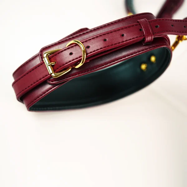 A close-up view of a luxurious burgundy leather collar designed for bed restraints, featuring a smooth, glossy finish. The collar is secured with a gold metal buckle and ring, allowing for easy adjustment and a secure fit. Subtle stitching details run along the edges, adding an elegant touch to the design. The inside of the collar is lined with a soft black material, enhancing comfort. Displayed on a light background, this stylish piece exemplifies sophisticated bed restraints set, perfect for those looking to explore intimacy with a blend of functionality and aesthetics.