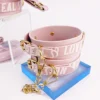 A pair of playful pink handcuffs from an electro-stimulation bed restraints set, featuring stylish "PASSION" and "LOVE" text along the straps. The cuffs are made from soft leather and are adorned with gold metal hardware, including adjustable buckles and clips. A connecting gold chain links the cuffs together, showcasing both functionality and aesthetic appeal. Displayed on a vibrant blue acrylic base, the cuffs rest against a clean white background, emphasizing their charming design. This eye-catching piece perfectly represents modern bed restraints set, ideal for adventurous intimate explorations.