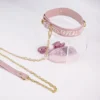 A stylish pink collar from an electro-stimulation bed restraints set, featuring the words "PASSION APPEAL" elegantly embossed along the strap. The collar is crafted from soft leather and is secured with gold metal buckles for a snug fit. Attached to the collar is a gold chain that connects to a matching leash, showcasing a combination of functionality and chic design. A pink control unit is partially visible in the background, hinting at the collar's electro-stimulation features. Displayed on a clear acrylic stand against a clean white background, this striking piece exemplifies modern bed restraints set, perfect for exploring intimate adventures with style.