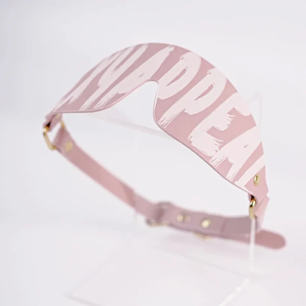 A chic pink eye mask from an electro-stimulation bed restraints set, featuring bold "SPOILED" text printed in a playful font across its surface. The mask has a smooth, glossy finish and is designed to comfortably cover the eyes while enhancing sensory play. It includes a soft adjustable strap with gold metal hardware, ensuring a secure fit. Displayed on a clear acrylic stand against a clean white background, this eye mask is a stylish piece of bed restraints set, perfect for those looking to explore intimacy and excitement with a touch of elegance and flair.