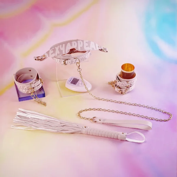 An array of stylish Electric Shock bed restraints set from an electro-stimulation bed restraints set elegantly arranged against a soft, pastel background. The centerpiece is a sleek pink collar reading "SEXY APPEAL," showcased on a clear stand. Flanking it are matching handcuffs with gold metal accents and chains. A unique leather flogger with smooth white strands and a gripping handle sits in the foreground, while a small remote control lies nearby. Each piece beautifully blends functionality with playful design, making this collection a perfect representation of modern bed restraints set for adventurous intimate experiences.