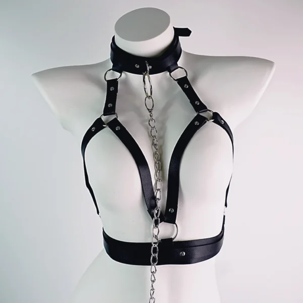 A striking black leather harness designed for bondage, displayed on a mannequin against a clean white background. The harness features multiple adjustable straps that elegantly outline the shoulders and chest, connecting to a wide collar. A decorative chain dangles from the front, adding an eye-catching element to the design. Silver metal accents and rings enhance the overall aesthetic, blending functionality with style. This sophisticated piece is a perfect example of modern bondage gear, ideal for those looking to explore their playful side in intimate settings.