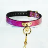 A vibrant restraint collar featuring a beautiful gradient of pink hues, transitioning to a shimmering gold. The collar is crafted from high-quality leather with a textured snakeskin design. It is secured with a gold metal buckle and showcases a central D-ring for versatility, perfect for attaching a leash or other accessories. A matching gold chain extends from the D-ring, adding an elegant touch. Displayed on a clear acrylic stand against a soft white background, this stunning piece exemplifies stylish restraint collar gear, ideal for those looking to explore intimacy with a blend of elegance and playfulness.