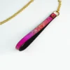 A stylish restraint collar with a stunning gradient design, featuring vibrant shades of pink transitioning into a deep black. The collar includes a shiny black leather backing with a textured snakeskin pattern on the front. Attached to the collar is a gold chain and a decorative ring, allowing for versatile use. The overall aesthetic combines elegance with edginess, perfect for those exploring intimate gear. Displayed against a clean white background, this beautiful piece of restraint collar gear embodies a playful yet sophisticated approach to restraint accessories.