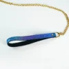 A close-up of a stylish BDSM collar attachment featuring a glossy blue and purple snakeskin-patterned strap that leads to a shiny gold chain. The strap has a black underside for added comfort, with a polished gold ring at the end for easy connection to a collar or leash. Displayed against a clean white background, this eye-catching accessory perfectly embodies modern restraint collar gear, combining playful elegance with functionality for those exploring intimate adventures.