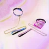 A vibrant display of colorful restraint collars arranged elegantly against a soft pastel background. The set includes a blue and purple glittery collar with a golden D-ring and matching chain, showcasing a chic design. Next to it, a pink collar with a similar glittery finish features gold accents and a sturdy clip. The brightly colored accessories reflect light beautifully, emphasizing their playful charm. This eye-catching arrangement perfectly embodies modern restraint collar and restraint collar gear, suitable for those looking to explore intimate adventures with style and flair.